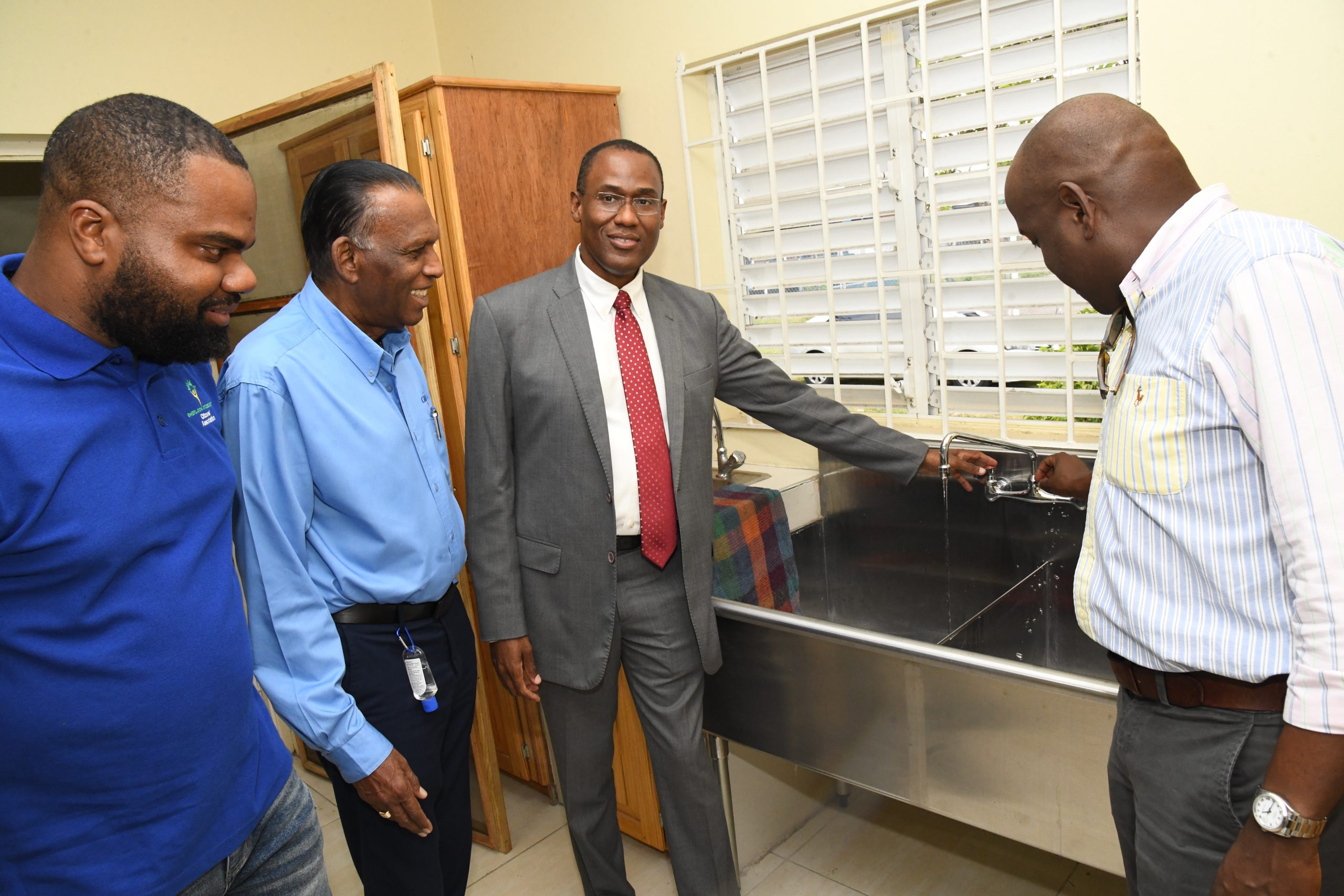 Dr. the Hon. Nigel Clarke, Minister of Finance and the Public Service and Member of Parliament for Northwest St. Andrew, tests the water pressure in the kitchen of the Sherlock Community Cultural Centre during a tour of the Centre after it was officially opened on April 20, 2023. With him are (left to right) Toushane Green, President of the Sherlock Citizens Association; W. Billy Heaven, CEO of the CHASE Fund and Councillor for the Chancery Division and Director of the CHASE Fund, Duane Smith.